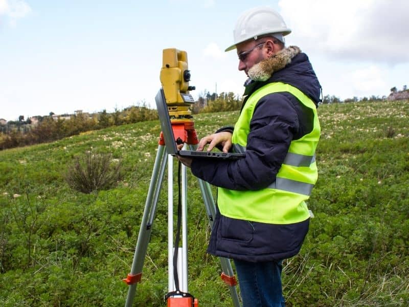 Surveyor measuring slope elevations with topographic survey equipment on a foothill lot before home site planning.
